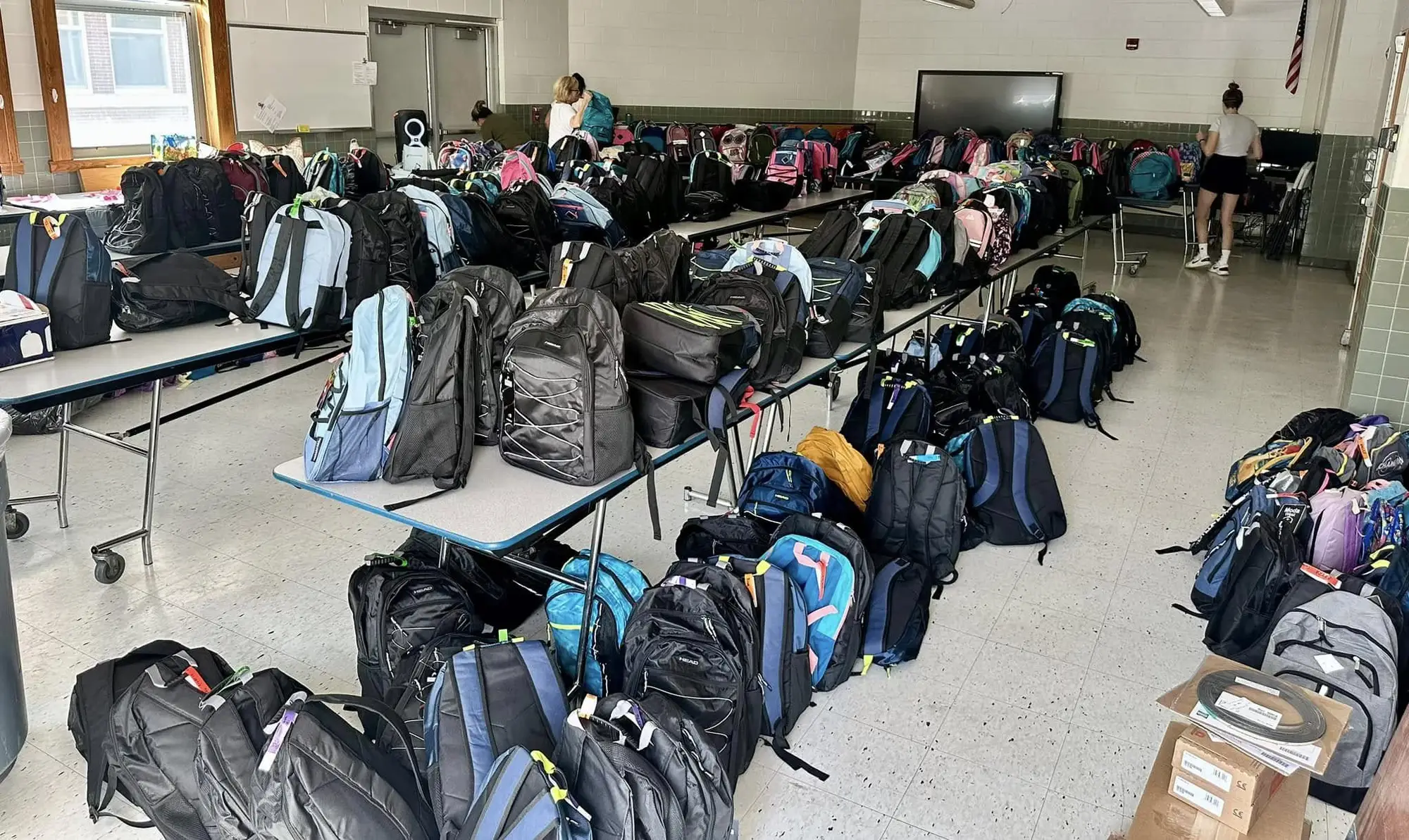 Hundreds of donated backpacks lined up in a school cafeteria