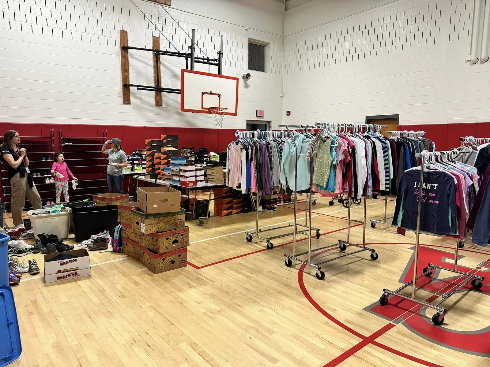 Families choosing free clothes and sneakers in a school gym